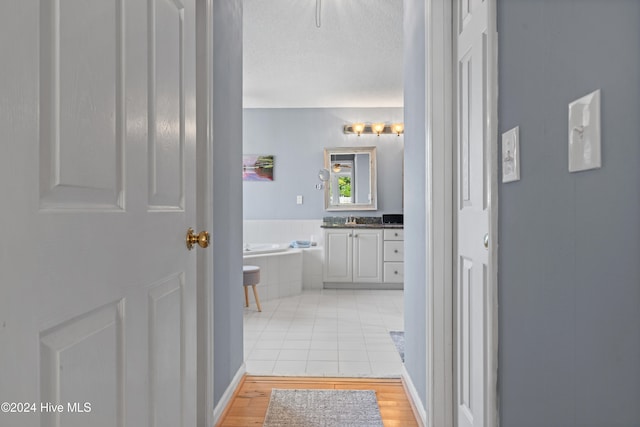 bathroom with a textured ceiling, vanity, hardwood / wood-style floors, and tiled bath