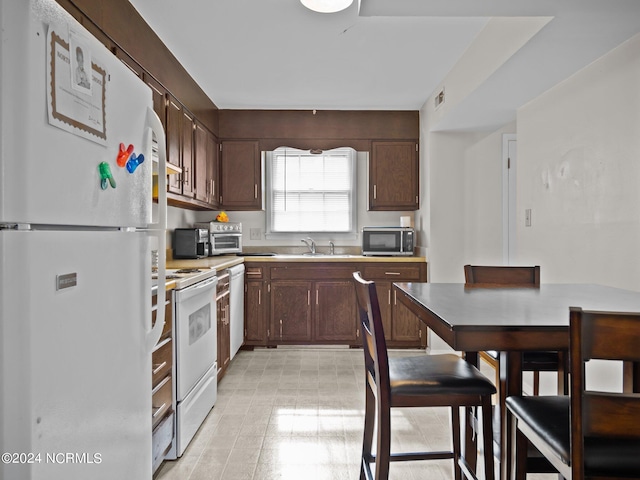 kitchen featuring dark brown cabinetry, white appliances, and sink