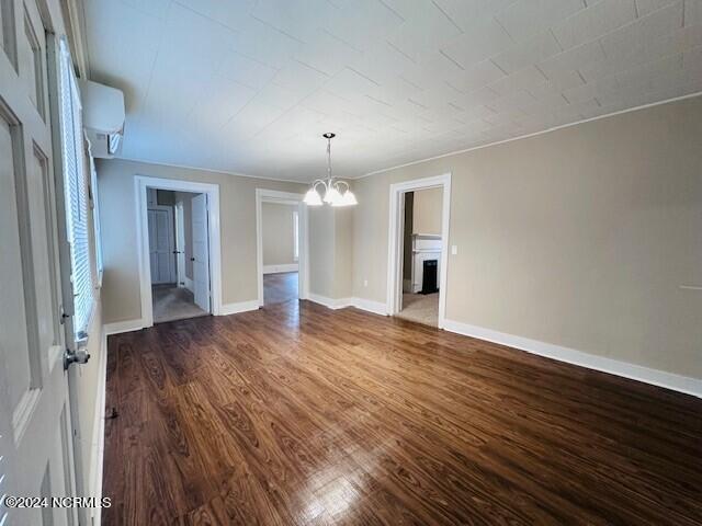 unfurnished living room featuring an AC wall unit, dark wood-type flooring, and a chandelier