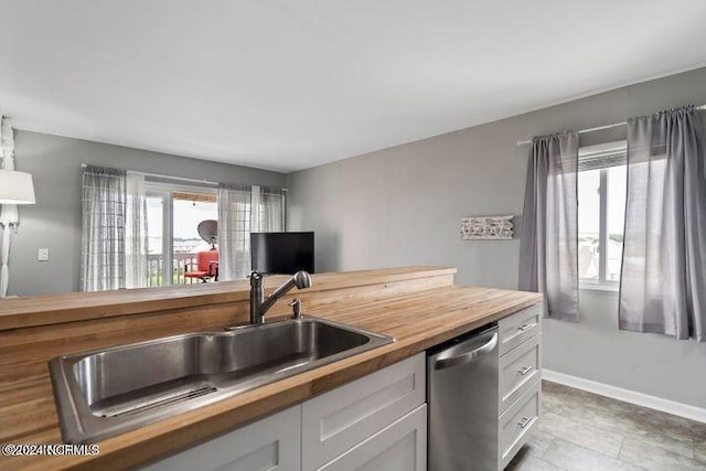 kitchen with white cabinets, butcher block counters, sink, light tile patterned flooring, and dishwasher