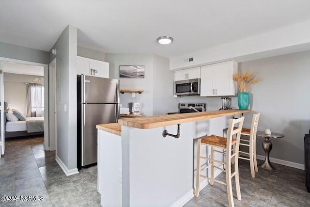 kitchen featuring white cabinets, stainless steel appliances, a kitchen bar, and butcher block counters