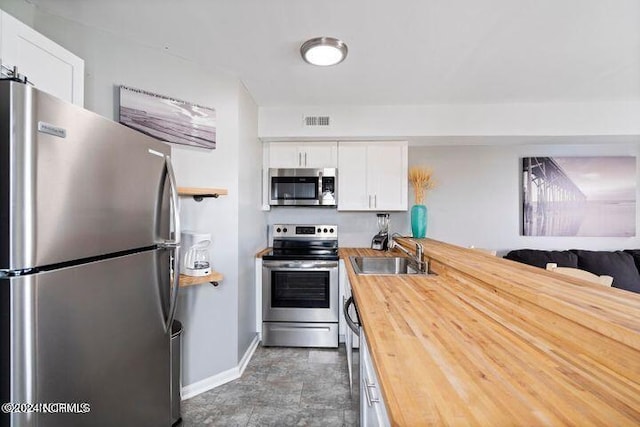 kitchen with stainless steel appliances, wooden counters, sink, and white cabinetry