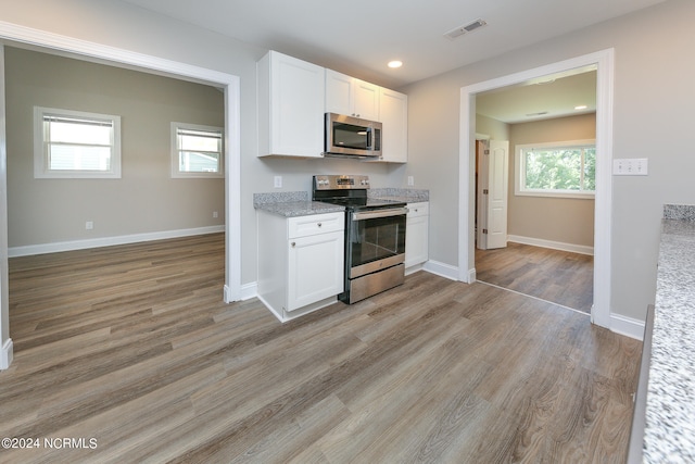 kitchen with a wealth of natural light, white cabinetry, light hardwood / wood-style floors, and appliances with stainless steel finishes