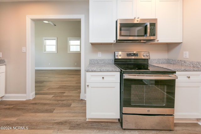 kitchen featuring white cabinets, stainless steel appliances, light wood-type flooring, and light stone countertops