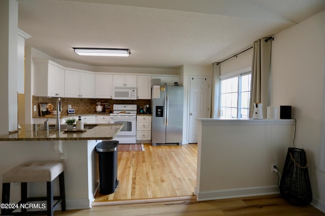 kitchen with dark stone counters, light hardwood / wood-style floors, white cabinetry, kitchen peninsula, and white appliances