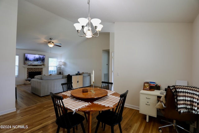 dining space with ceiling fan with notable chandelier, dark wood-type flooring, vaulted ceiling, and a tile fireplace