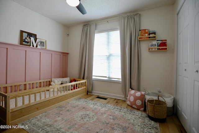 bedroom with a crib, ceiling fan, light hardwood / wood-style flooring, and a closet