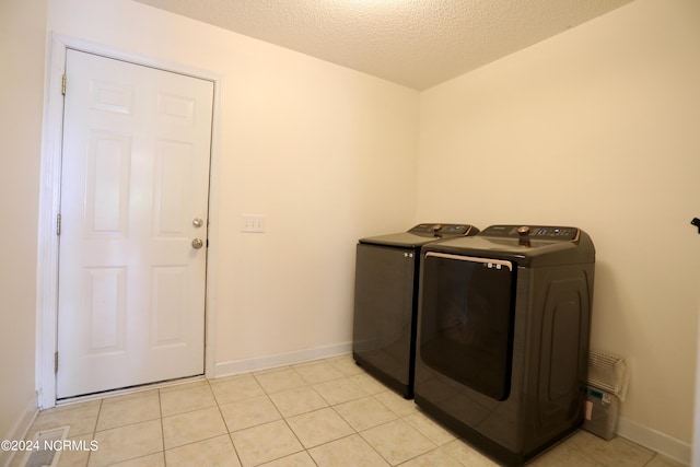 washroom with a textured ceiling, washing machine and dryer, and light tile patterned flooring