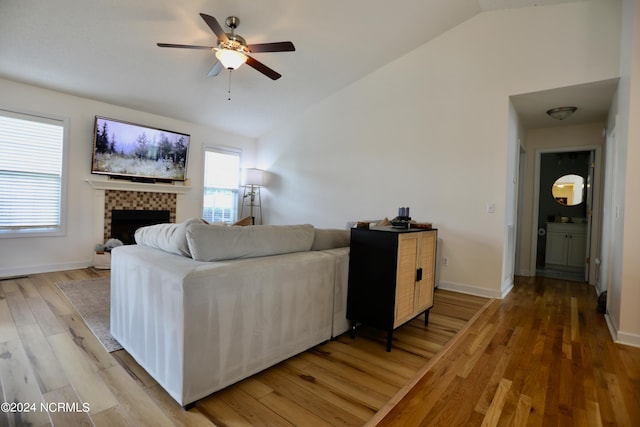 living room featuring lofted ceiling, light hardwood / wood-style floors, a tile fireplace, and ceiling fan