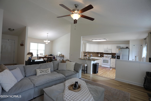 living room featuring ceiling fan with notable chandelier, lofted ceiling, and light hardwood / wood-style flooring