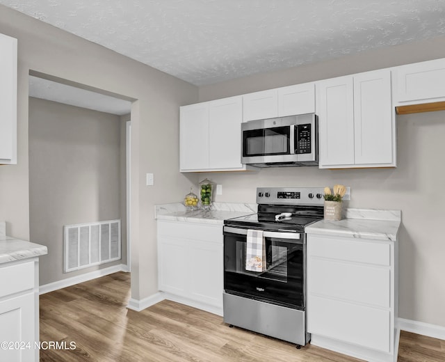 kitchen with white cabinets, appliances with stainless steel finishes, and light hardwood / wood-style flooring