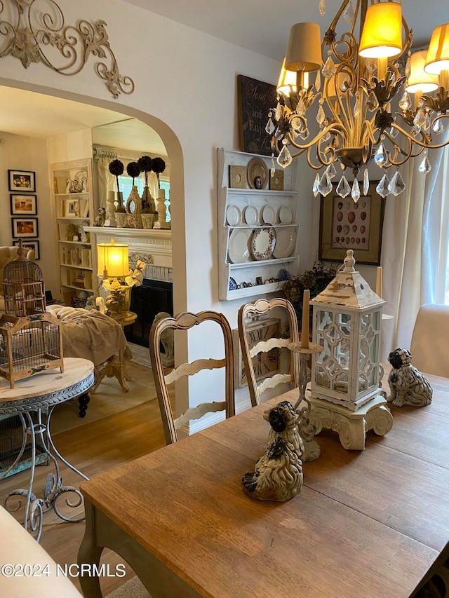 dining room with wood-type flooring, a chandelier, and a brick fireplace