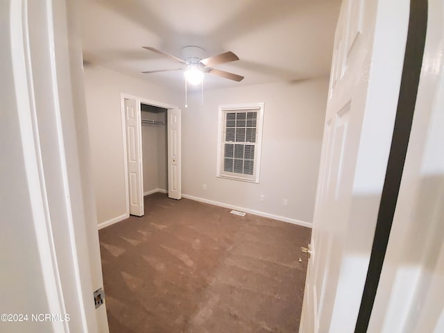 unfurnished bedroom featuring ceiling fan, a closet, and dark colored carpet