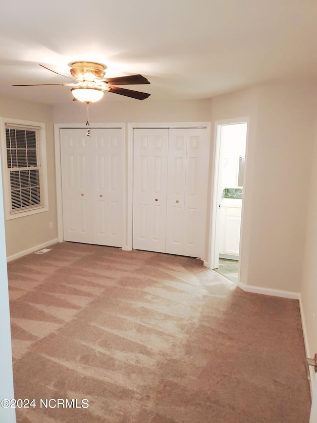 unfurnished bedroom featuring carpet flooring, multiple closets, and ceiling fan