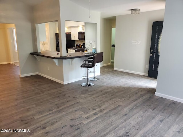 kitchen with a breakfast bar, kitchen peninsula, white cabinets, black appliances, and hardwood / wood-style flooring