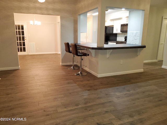 kitchen with hanging light fixtures, kitchen peninsula, black appliances, a kitchen breakfast bar, and dark hardwood / wood-style flooring