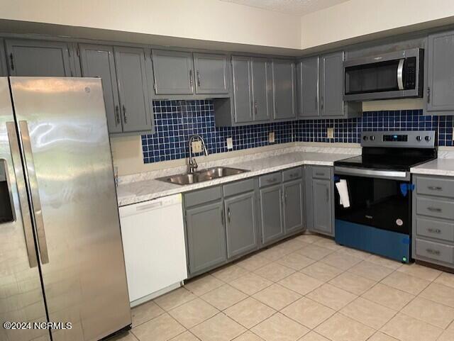 kitchen with sink, gray cabinetry, backsplash, light tile patterned floors, and stainless steel appliances