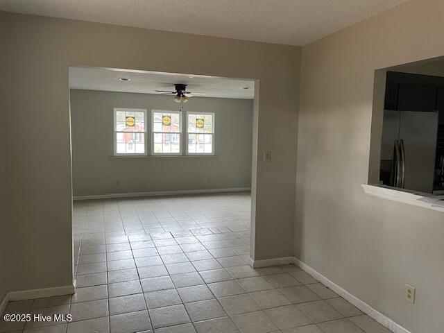 tiled empty room with ceiling fan and a textured ceiling