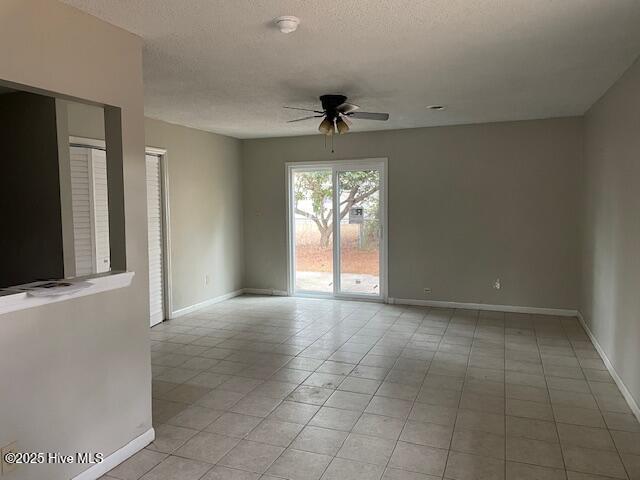 tiled empty room with ceiling fan and a textured ceiling