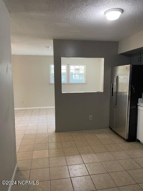 kitchen featuring stainless steel refrigerator with ice dispenser, light tile patterned flooring, white cabinets, and a textured ceiling