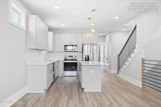 kitchen featuring appliances with stainless steel finishes, sink, hanging light fixtures, white cabinetry, and light hardwood / wood-style floors