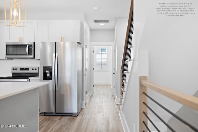 kitchen with white cabinetry, stainless steel appliances, decorative light fixtures, decorative backsplash, and light hardwood / wood-style flooring