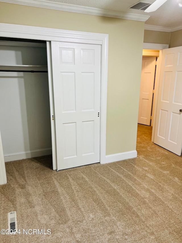 unfurnished bedroom featuring ceiling fan, a closet, crown molding, and carpet flooring