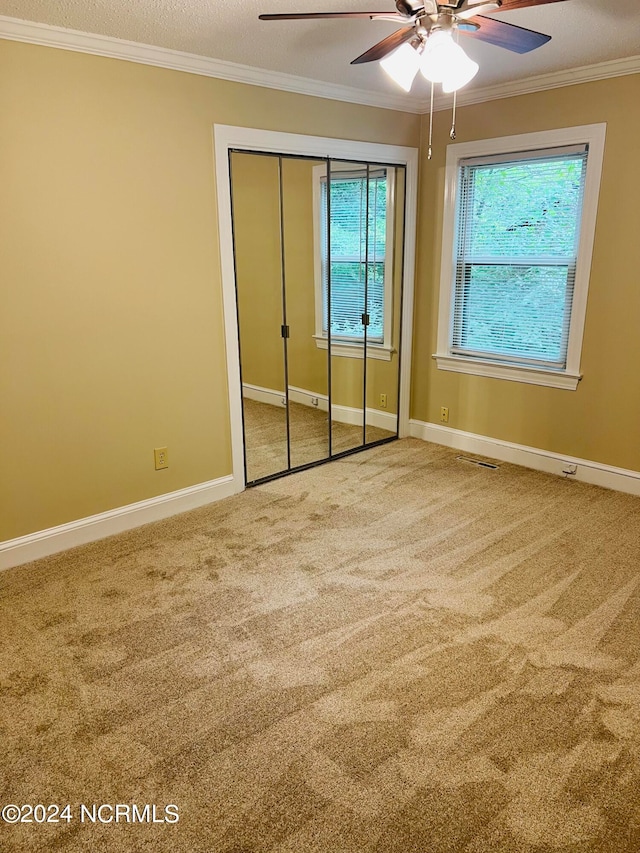 unfurnished bedroom with ceiling fan, ornamental molding, a closet, and carpet flooring