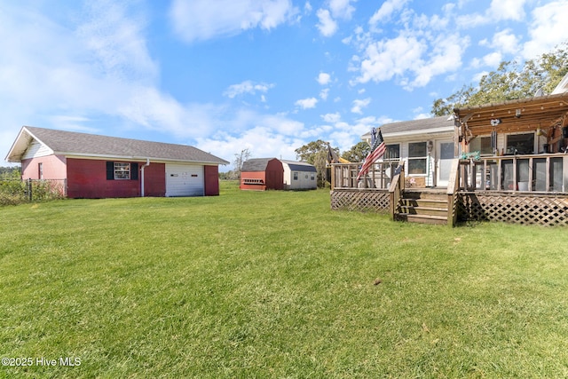 view of yard featuring a garage, a sunroom, fence, a deck, and an outdoor structure