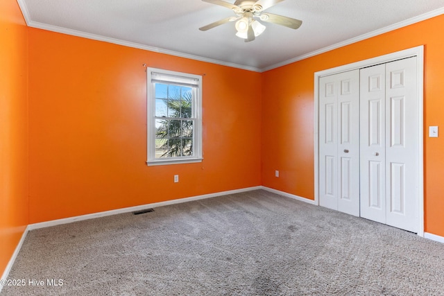 unfurnished bedroom with carpet floors, visible vents, baseboards, ornamental molding, and a closet