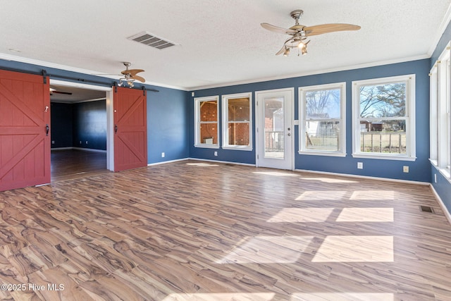 spare room featuring ornamental molding, a barn door, wood finished floors, and visible vents