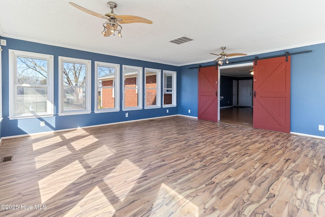 unfurnished living room with a barn door, a textured ceiling, crown molding, and a ceiling fan