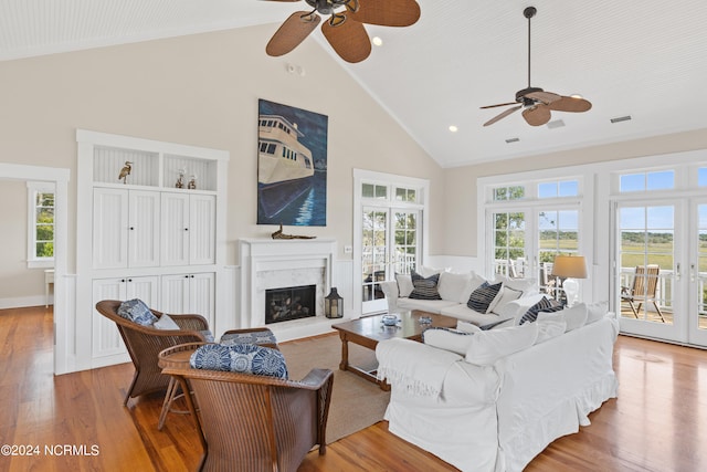 living room with high vaulted ceiling, ceiling fan, french doors, hardwood / wood-style floors, and a premium fireplace