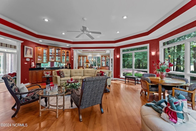 living area with ornamental molding, ceiling fan, light wood-type flooring, and a raised ceiling