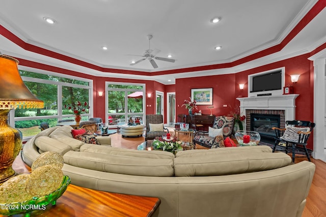 living room featuring light hardwood / wood-style floors, a brick fireplace, crown molding, a tray ceiling, and ceiling fan