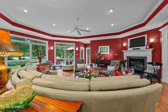 living area with a fireplace, wood finished floors, ceiling fan, and ornamental molding