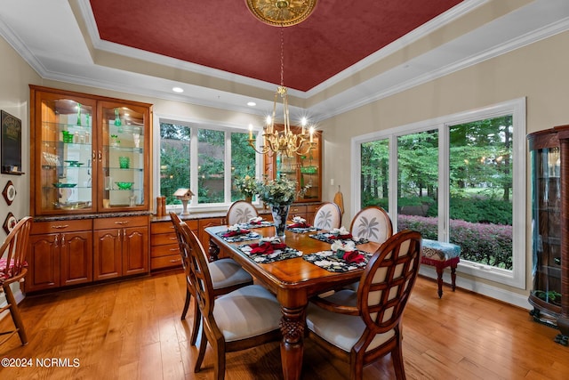 dining space with an inviting chandelier, a raised ceiling, crown molding, and light hardwood / wood-style floors