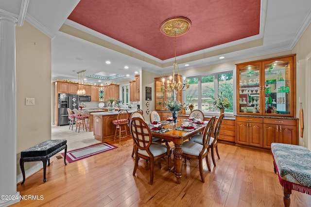 dining space with an inviting chandelier, a raised ceiling, light hardwood / wood-style flooring, and ornamental molding