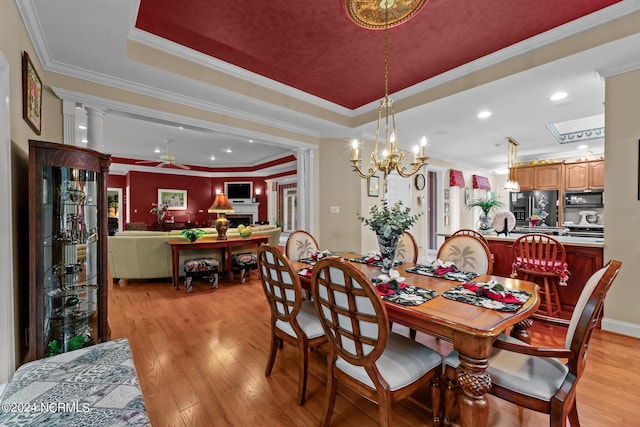 dining area with light wood finished floors, ceiling fan with notable chandelier, ornamental molding, and a raised ceiling