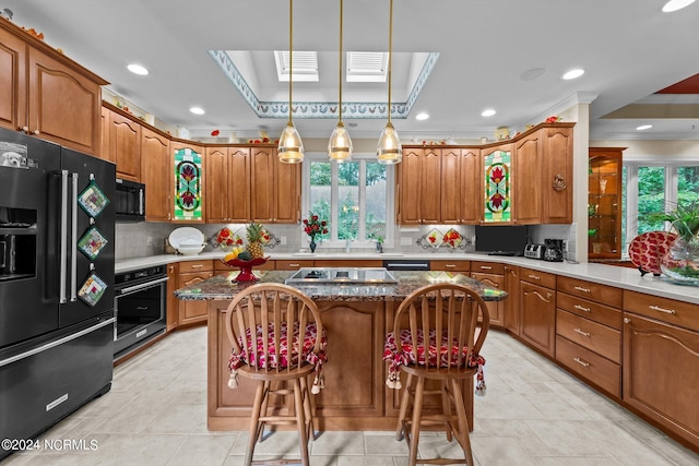 kitchen featuring brown cabinets, black appliances, a center island, a skylight, and decorative backsplash