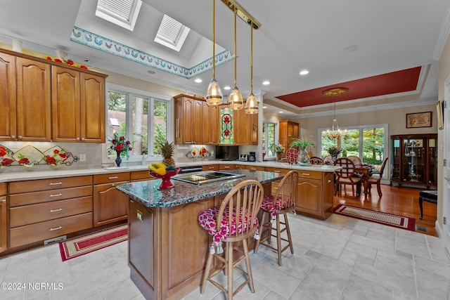 kitchen featuring brown cabinets, a tray ceiling, a kitchen island, tasteful backsplash, and a peninsula