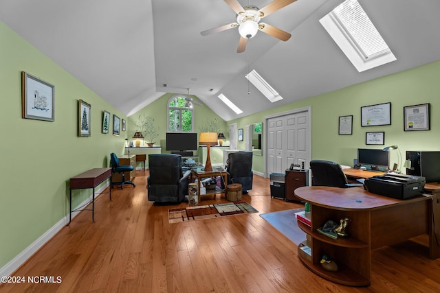 home office featuring a ceiling fan, vaulted ceiling with skylight, baseboards, and hardwood / wood-style floors