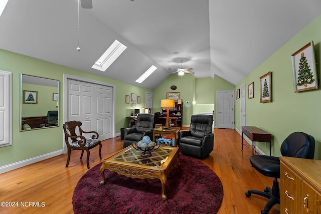 living area featuring lofted ceiling with skylight, baseboards, light wood finished floors, and ceiling fan