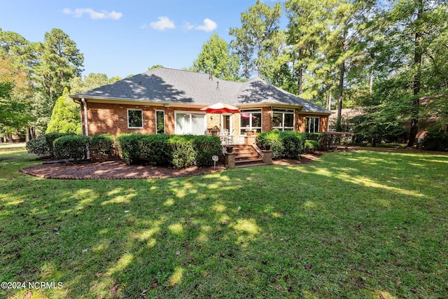 back of house with a lawn, brick siding, and roof with shingles