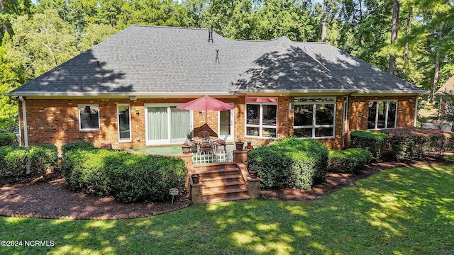back of house featuring roof with shingles, brick siding, and a yard