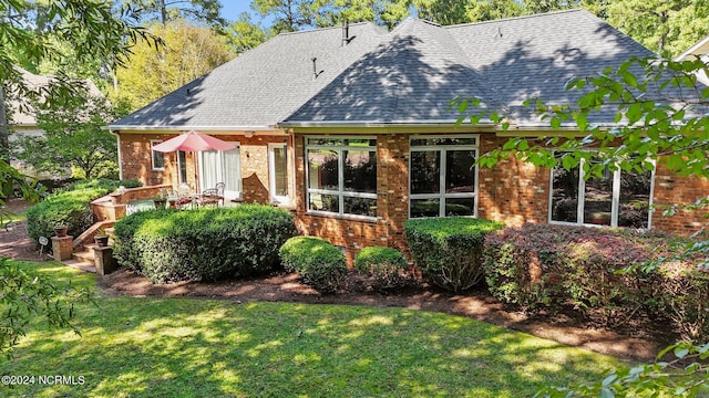 back of property featuring brick siding, roof with shingles, and a lawn