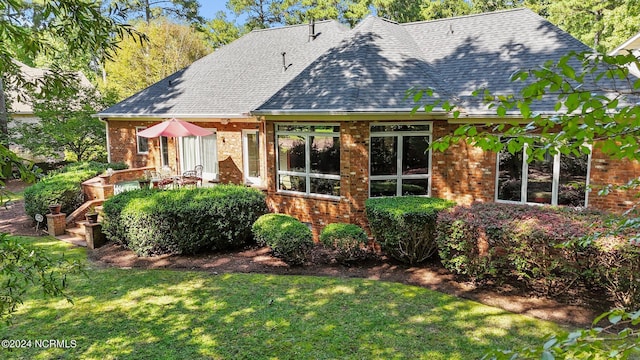 back of house featuring a lawn, a shingled roof, and brick siding