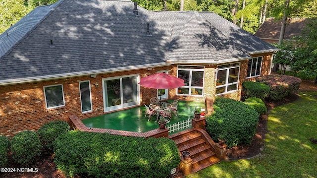 back of property featuring brick siding, a lawn, and roof with shingles