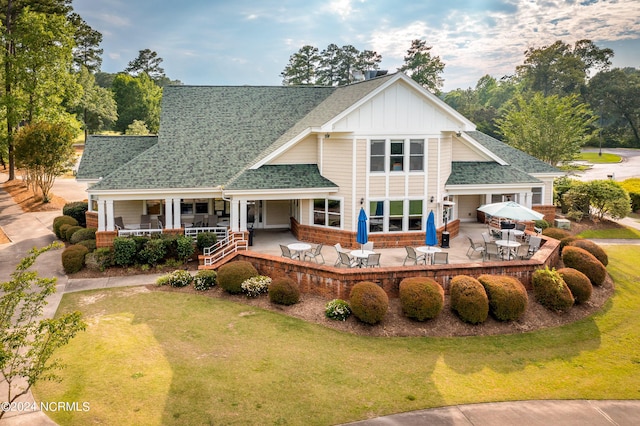 rear view of house with a patio, an attached garage, board and batten siding, a shingled roof, and a yard