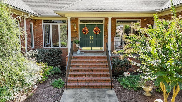 doorway to property with a porch, brick siding, and roof with shingles